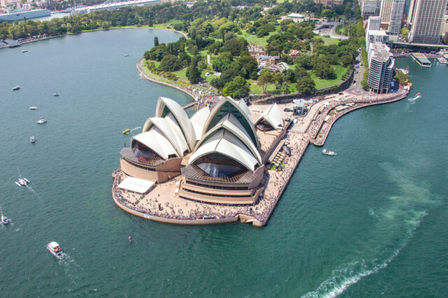 The Sydney Opera House sits on a peninsula, surrounded by water and people