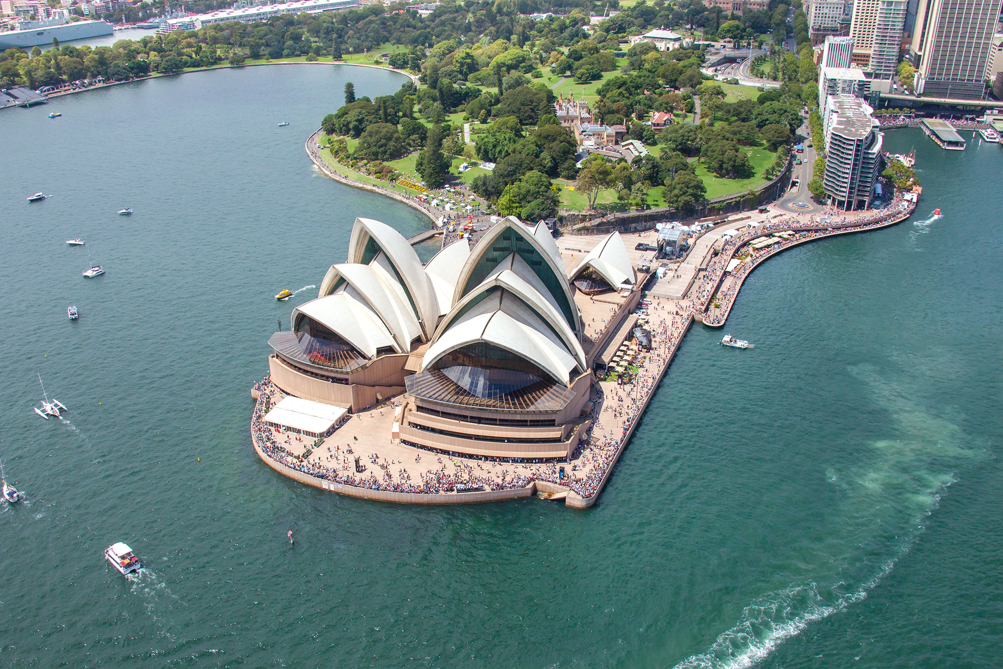 The Sydney Opera House sits on a peninsula, surrounded by water and people