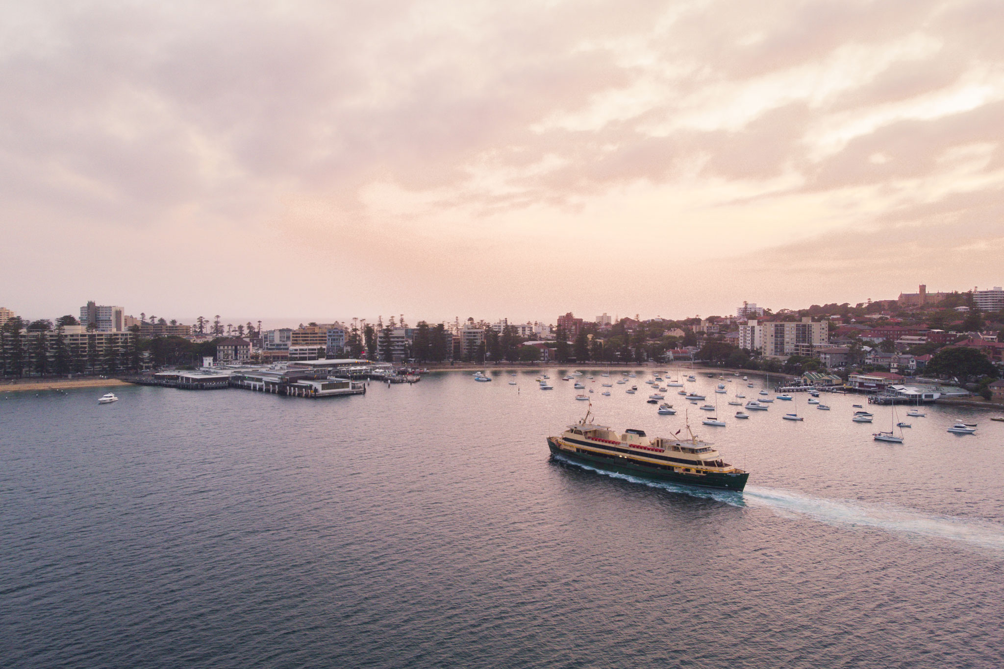 A ferry navigates a calm bay, passing a waterfront town at sunset