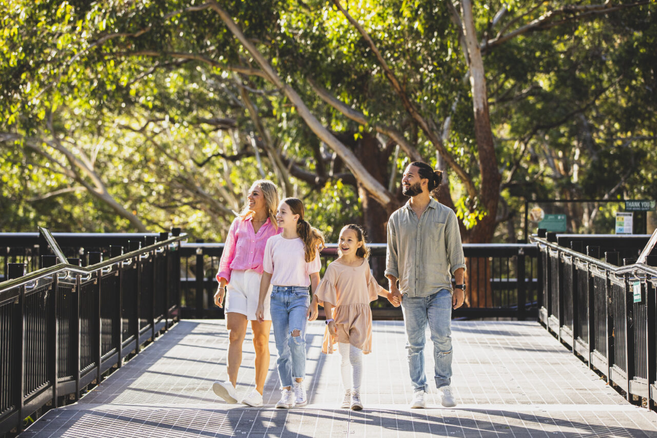 A family of four strolls along an elevated walkway, holding hands