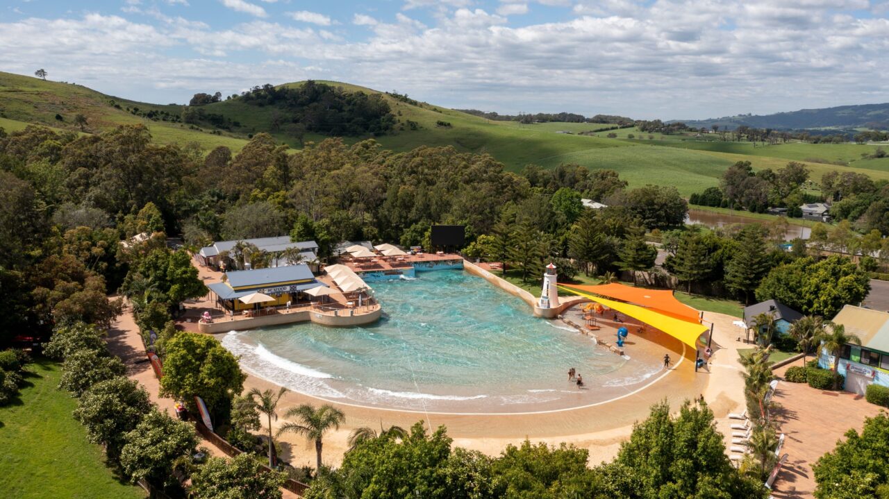 A wave pool generates artificial waves; people relax and play on the sandy beach surrounding it