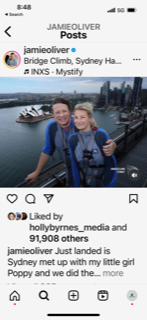 A couple smiles for a selfie atop a bridge; the Sydney Opera House is visible in the background