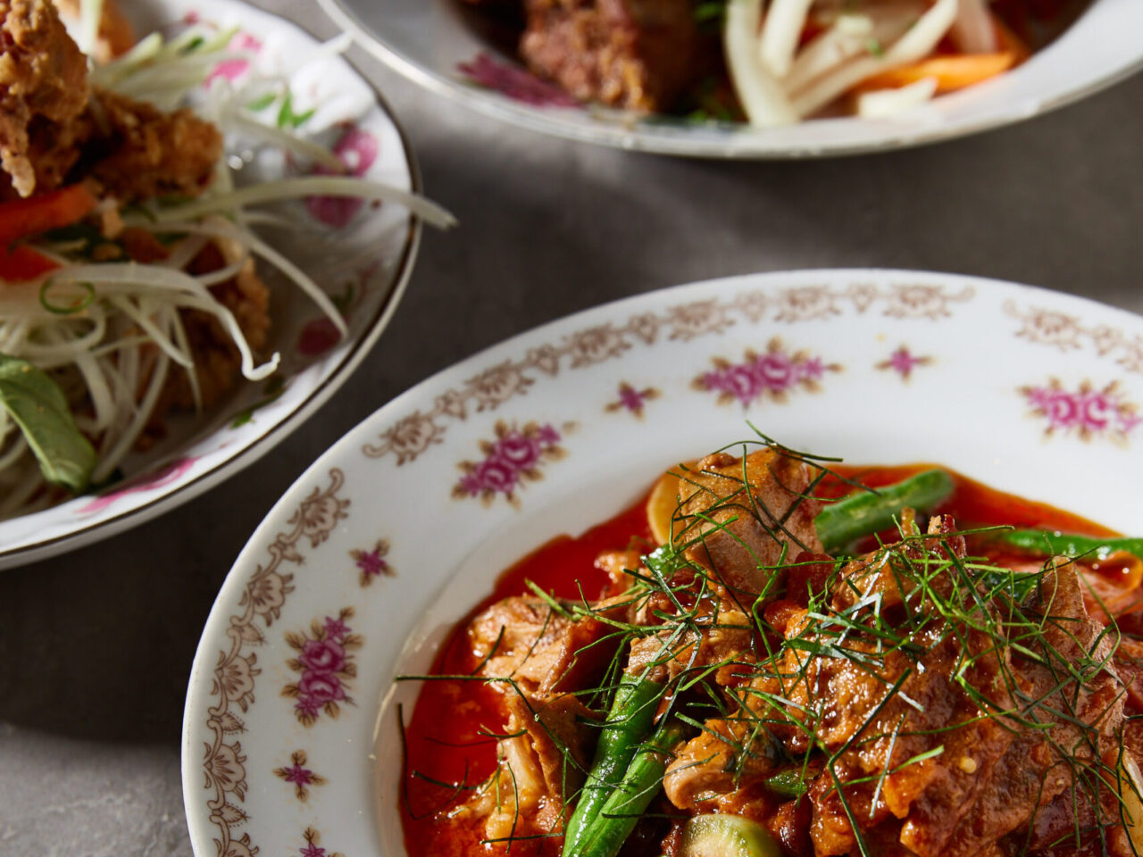 A red curry, garnished with herbs, sits on an ornate plate