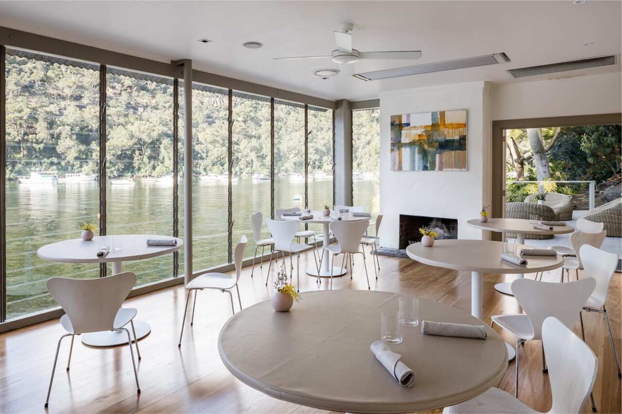 Round tables are set for dining in a light-filled waterfront restaurant