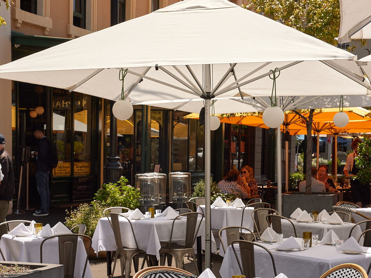 White umbrellas shade outdoor cafe tables with white linens