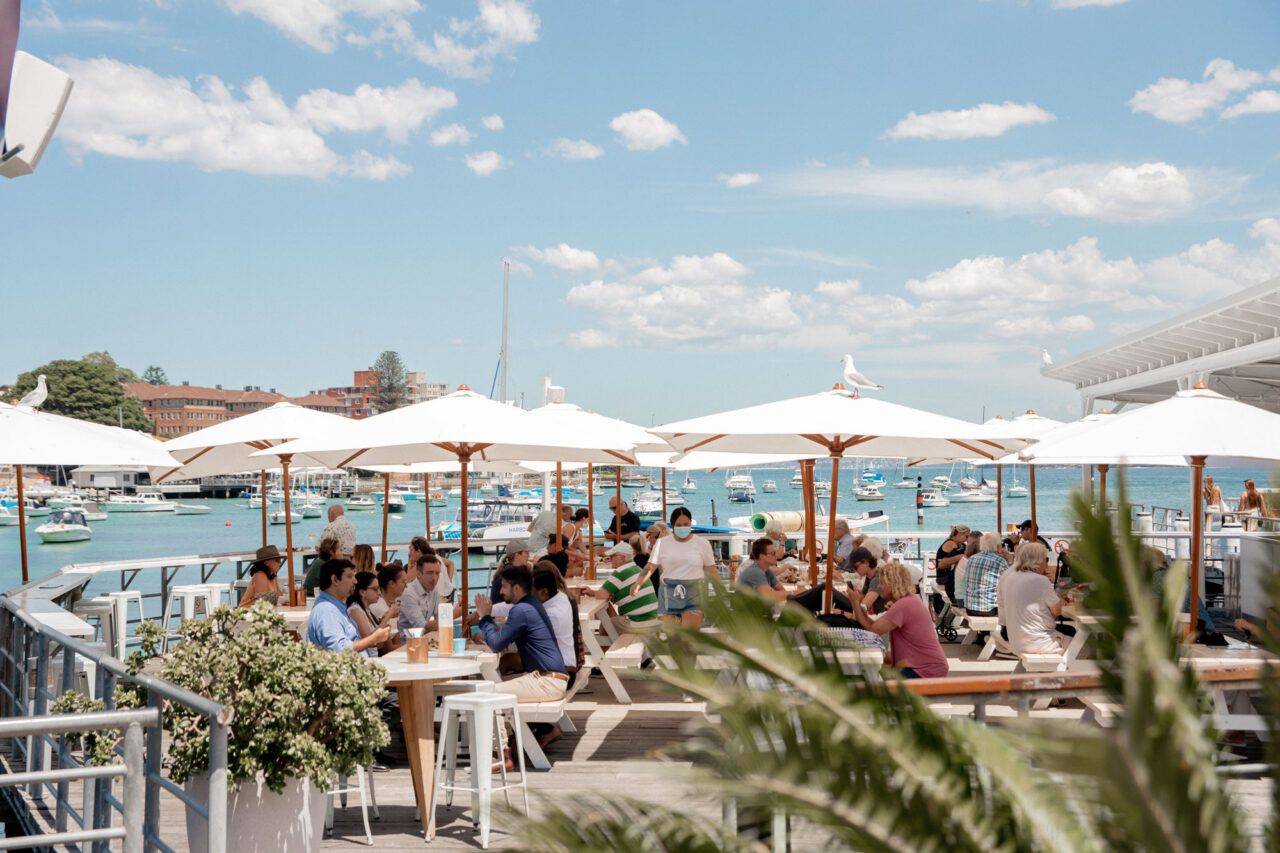 People dine under white umbrellas at an outdoor waterfront restaurant