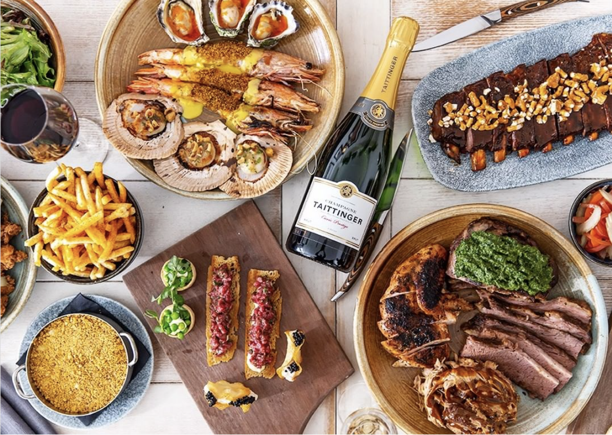Seafood, meats, and sides are arranged on a table; a bottle of Taittinger champagne is present