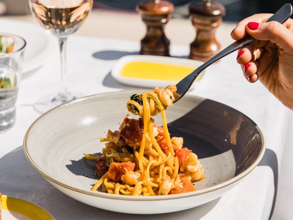 A fork lifts a portion of pasta with tomatoes and seafood from a gray bowl