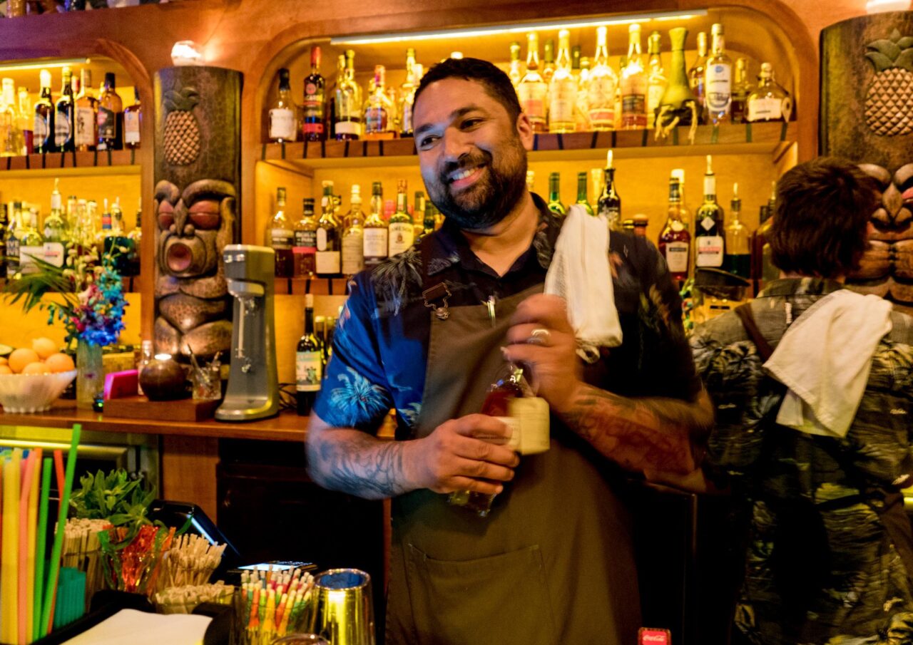 A bartender prepares a drink behind a bar stocked with liquor bottles