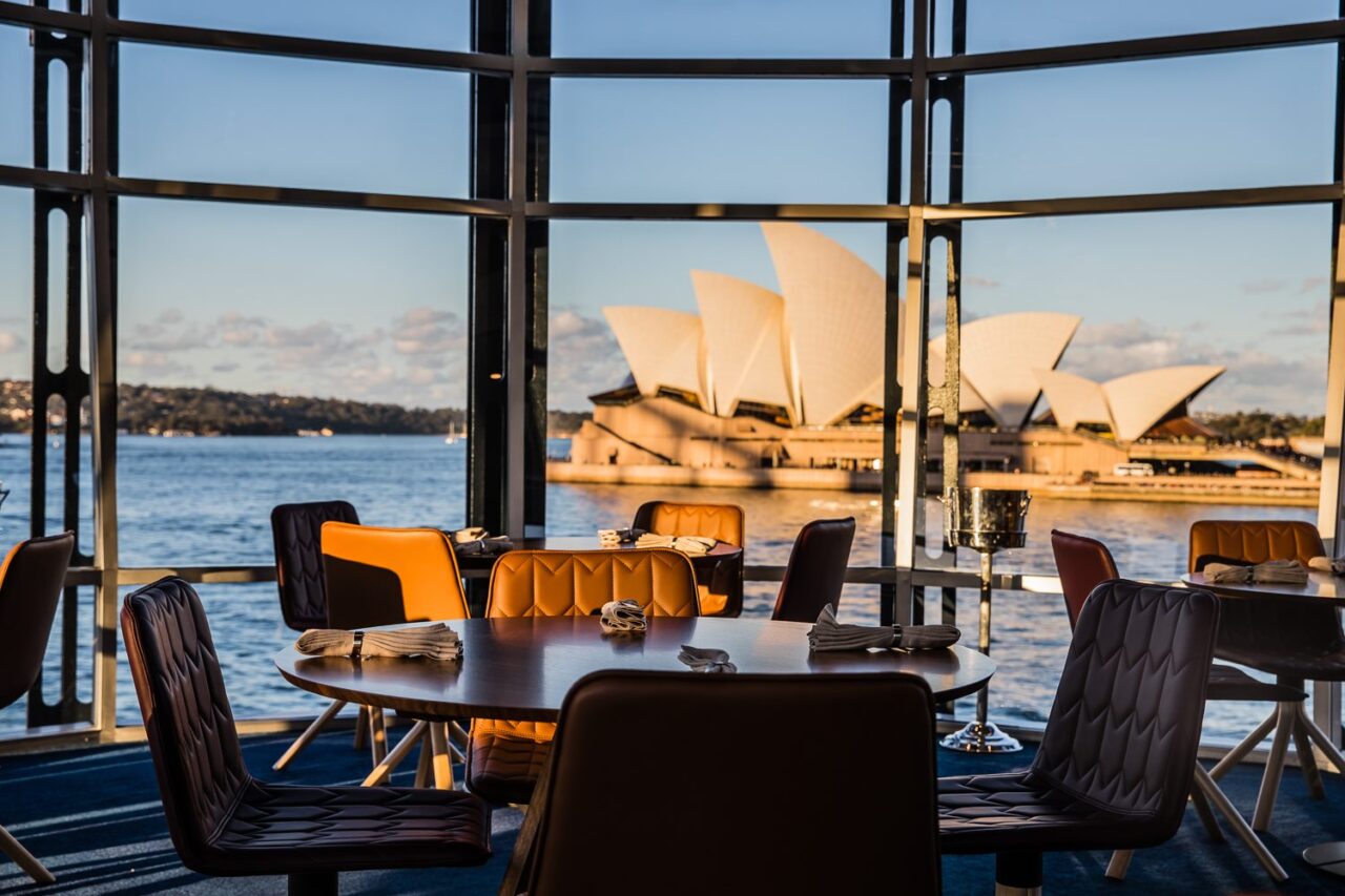 A restaurant table sits by a window overlooking the Sydney Opera House and harbor