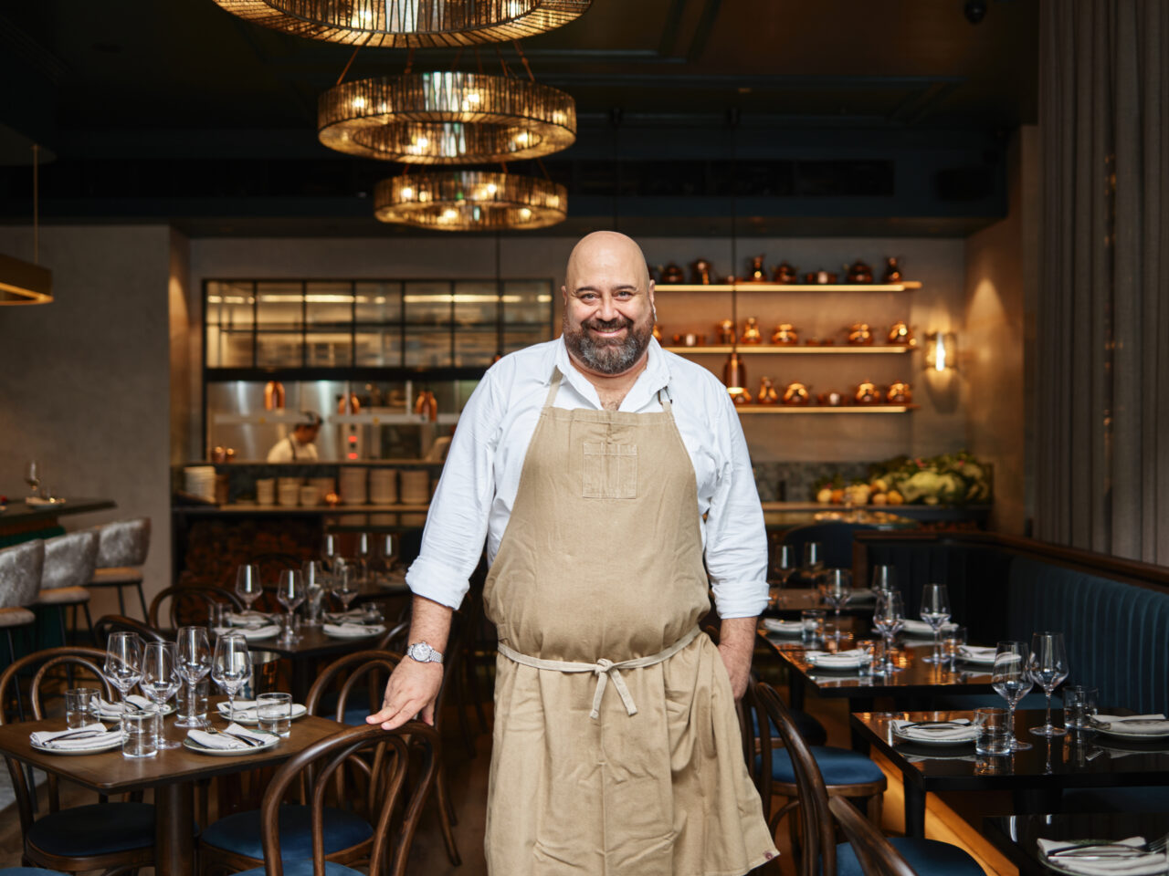 A chef stands proudly in a restaurant, hands resting on a table