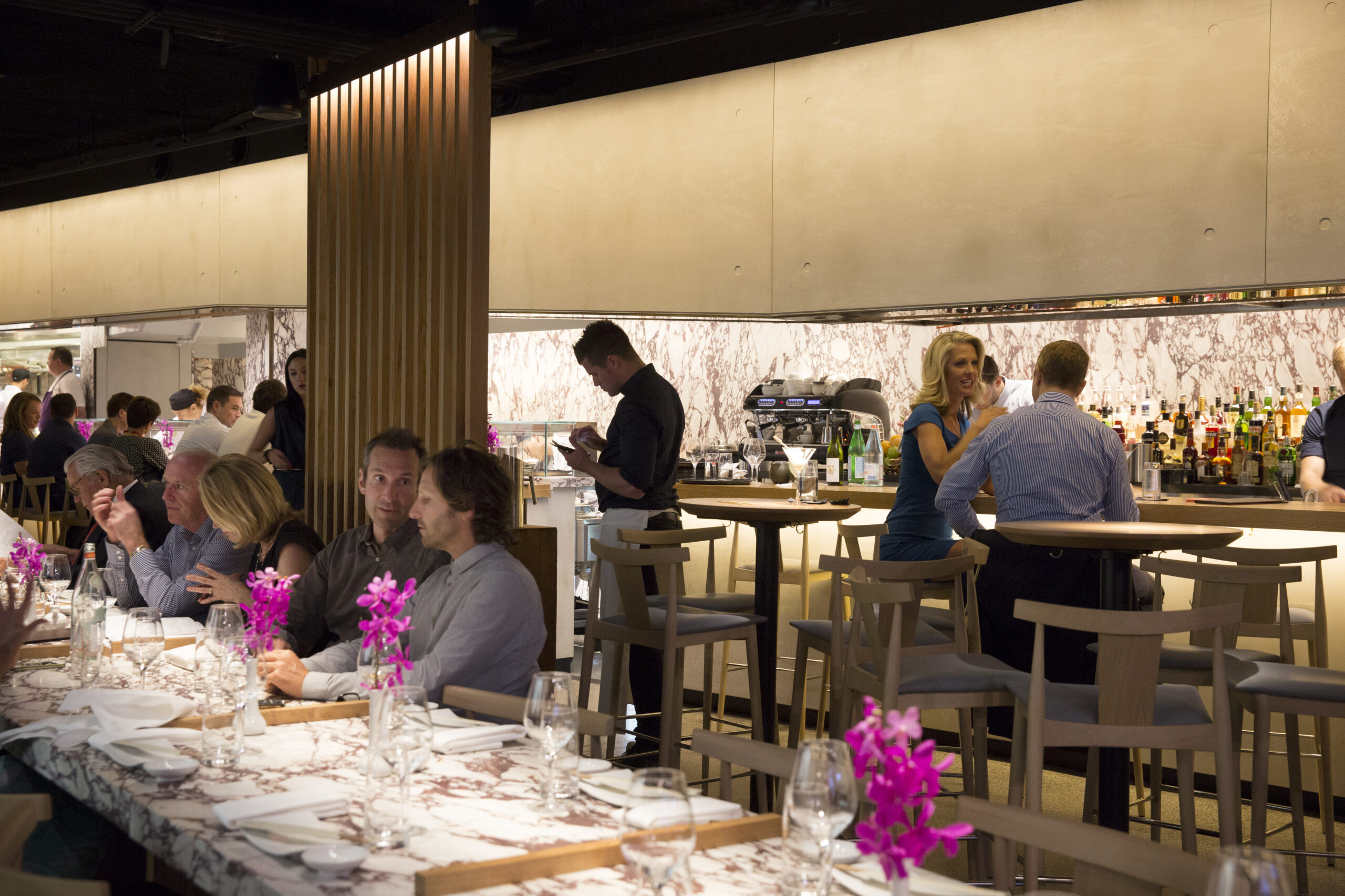 A long marble table is being used by diners in a restaurant