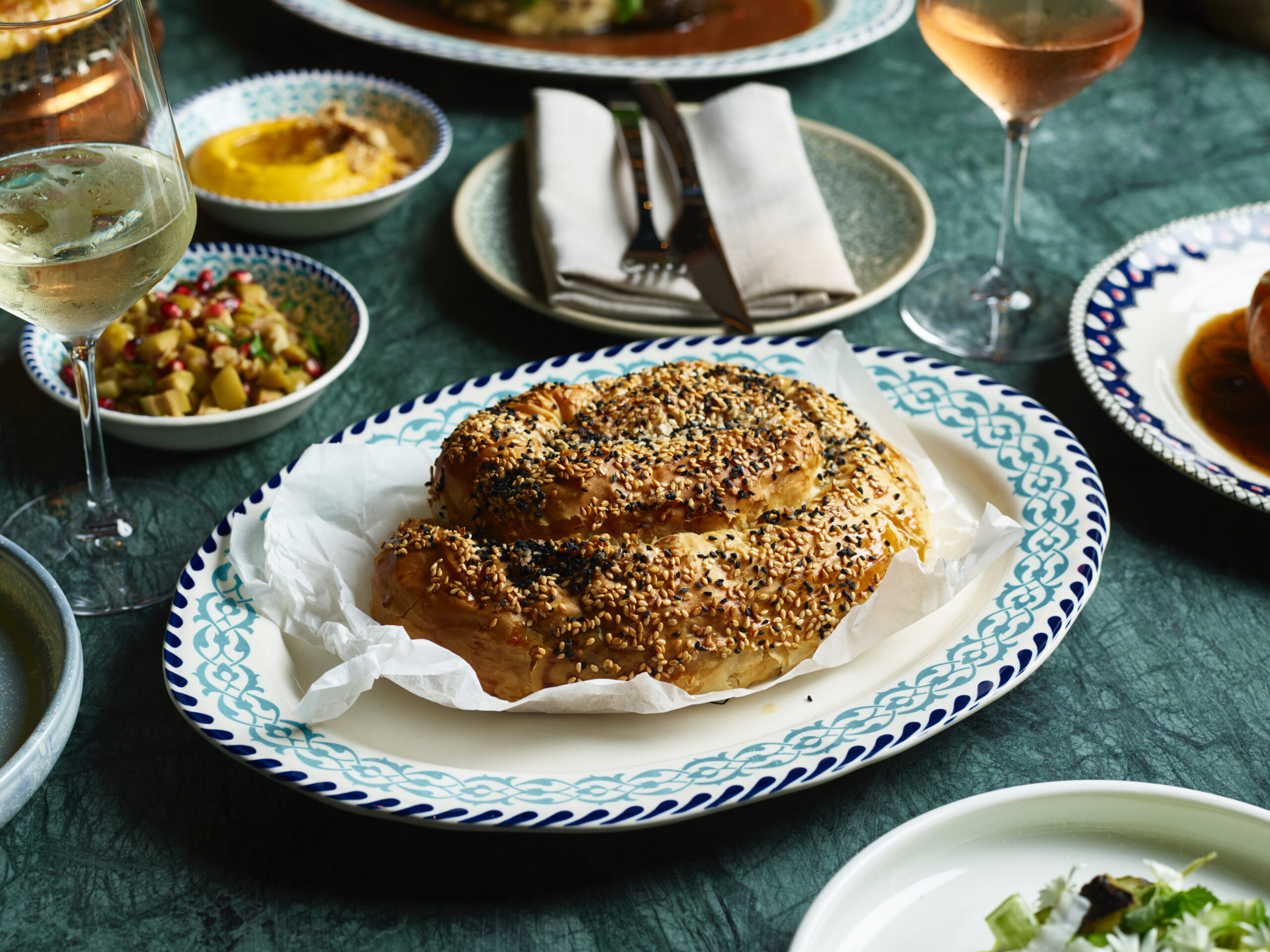 A pastry, topped with sesame seeds, rests on a patterned plate