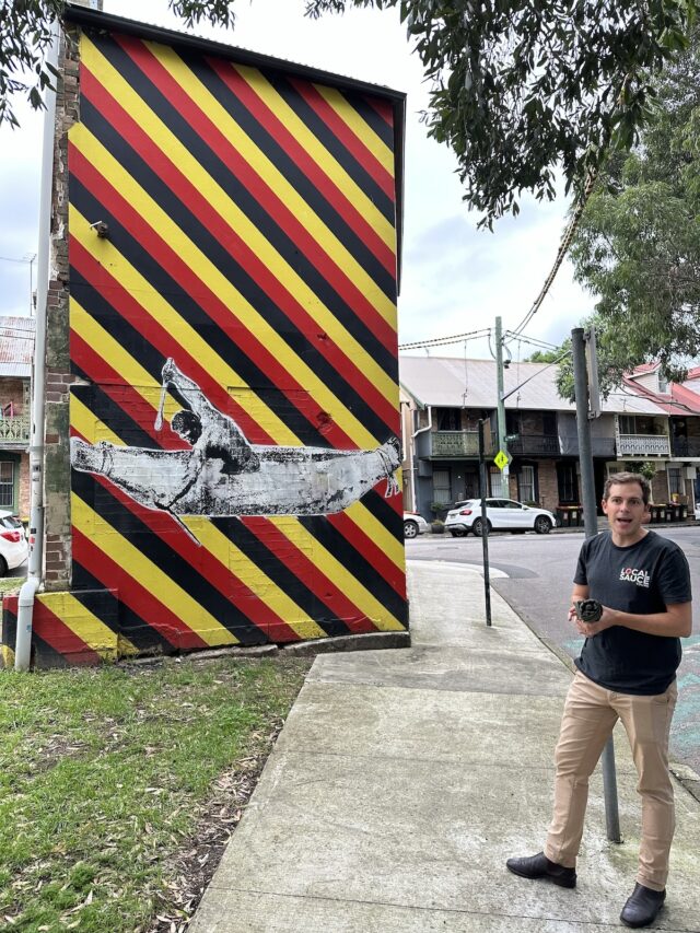 A mural depicting a person canoeing, painted on a building's exterior wall with diagonal stripes of red, yellow, and black