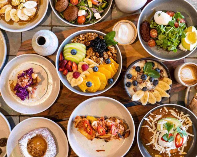 A variety of breakfast dishes—fruit bowls, pancakes, and savory plates—are arranged on a wooden table