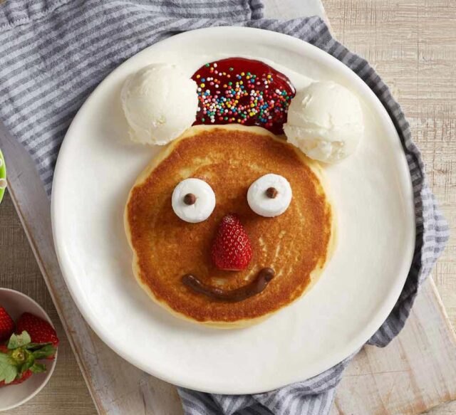 A pancake, decorated as a face with ice cream, is served on a plate