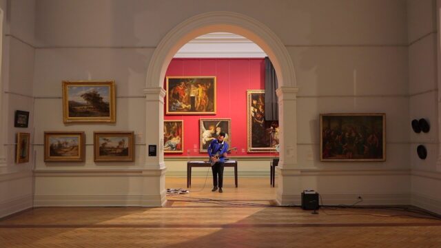 A person plays an electric guitar in a gallery