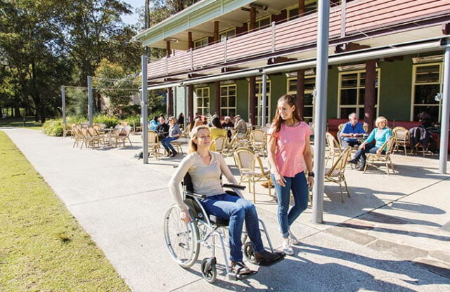 A woman in a wheelchair is being wheeled by another woman on a patio outside a building