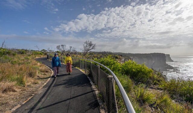 Two women walk along a paved coastal path