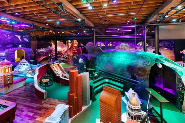 Miniature cityscapes and a submarine-like structure are incorporated into a vibrant, indoor mini-golf course