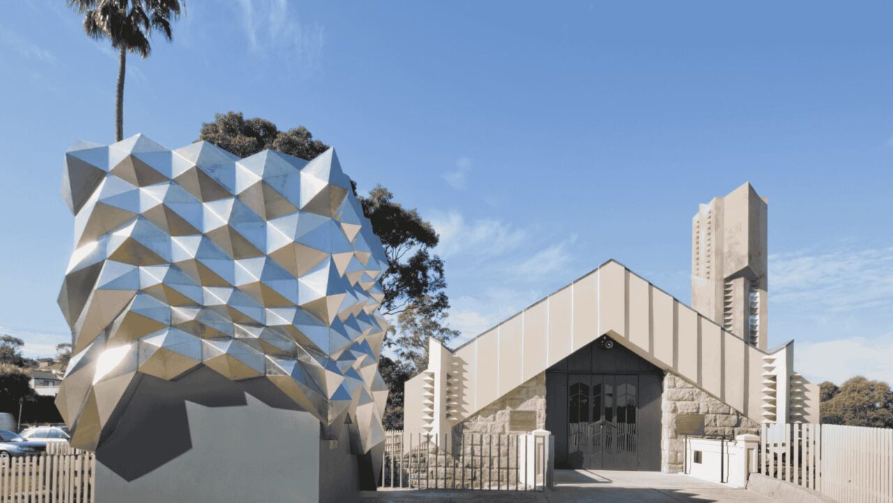 A faceted, metallic sculpture stands beside a tan