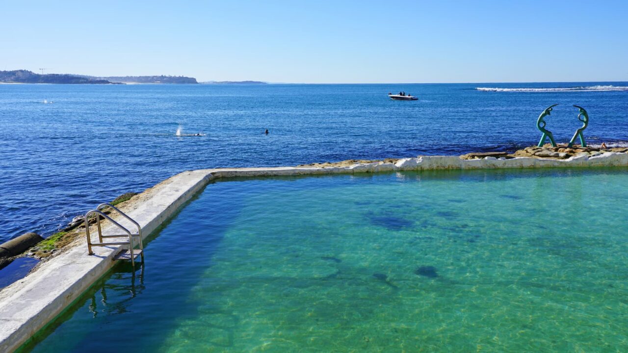 A clear, ocean-water pool sits adjacent to the sea, featuring a metal ladder