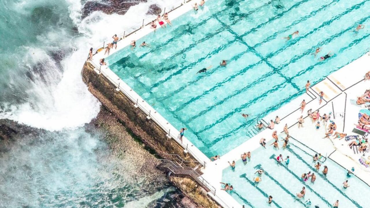 A large oceanside pool is filled with swimmers and sunbathers
