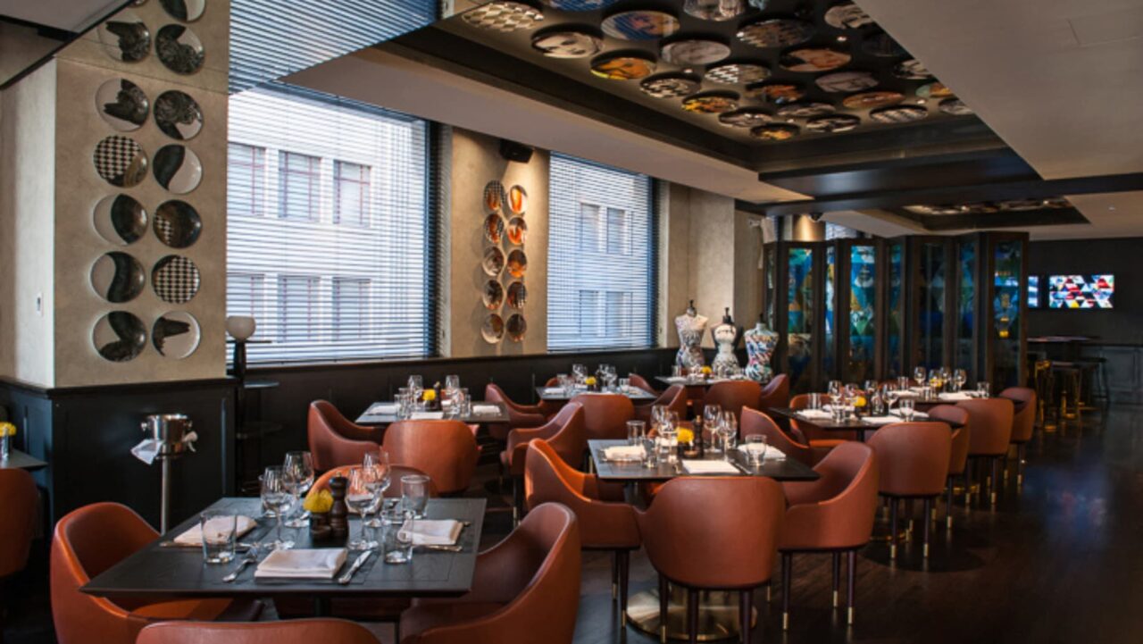 A restaurant's tables are set for diners, featuring orange chairs and dark tabletops