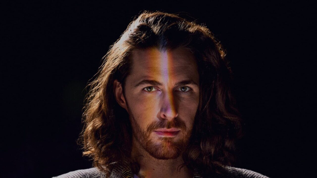 A man with long brown hair is looking directly at the camera