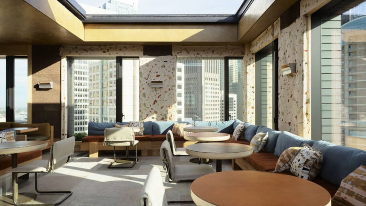 A rooftop lounge, featuring seating arrangements and small tables, overlooks a cityscape