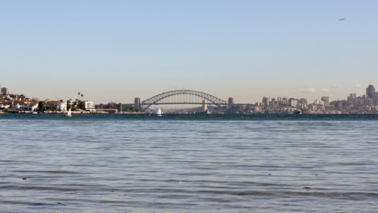 A sailboat floats on calm water, a distant arch bridge spans a bay