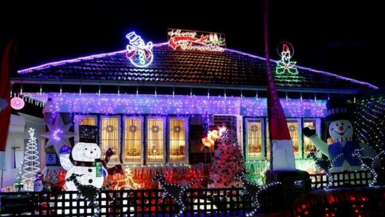 A house is decorated with numerous colorful Christmas lights and inflatable figures, including snowmen, creating a festive nighttime display