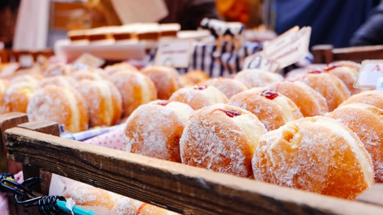 Many sugared doughnuts, filled with jam, sit in a wooden crate at a market