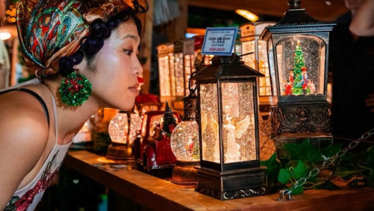 A woman examines illuminated snow globes; one depicts an angel, another a Christmas tree