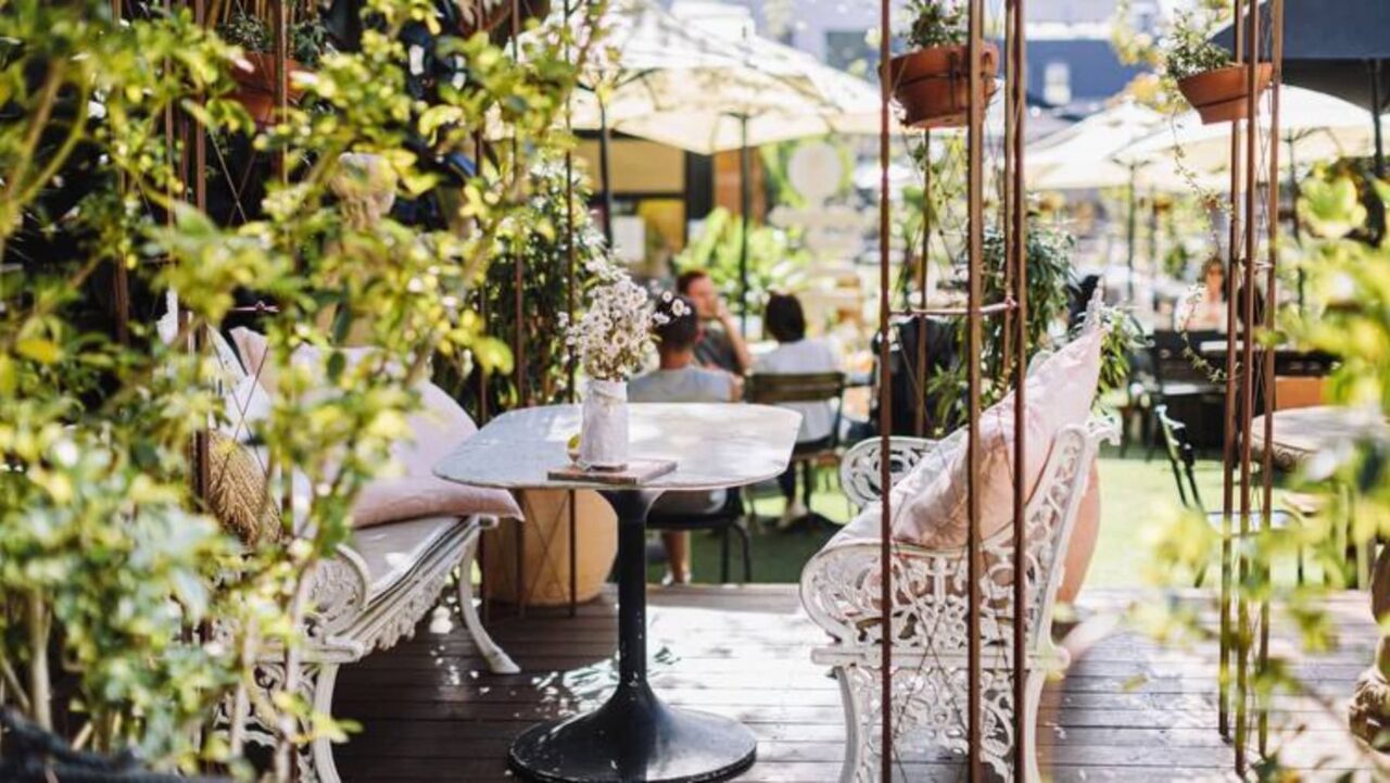 White metal benches sit on a patio, adorned with pink cushions