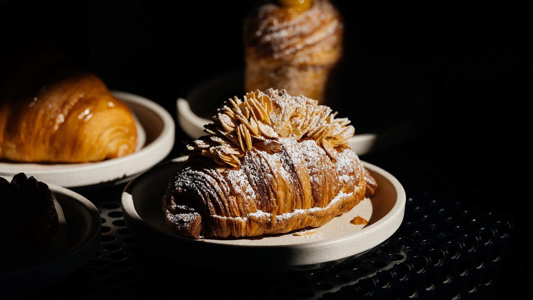 Almond croissant with powdered sugar on a plate with other pastries.