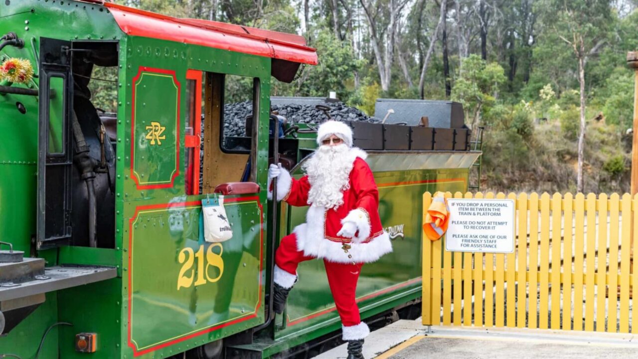A man in a Santa suit climbs onboard a green, yellow and red vintage steam train in the Blue Mountains near Sydney, Australia.