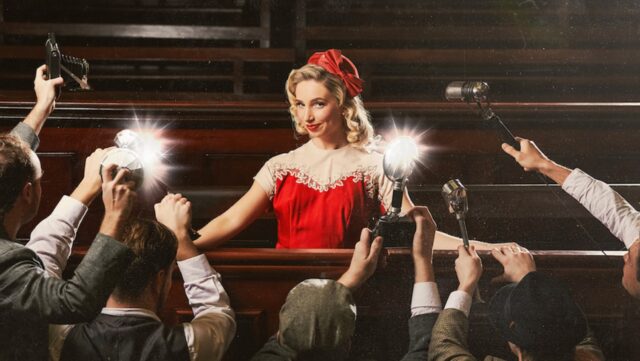 A woman in a red dress in a court room with cameras flashing.