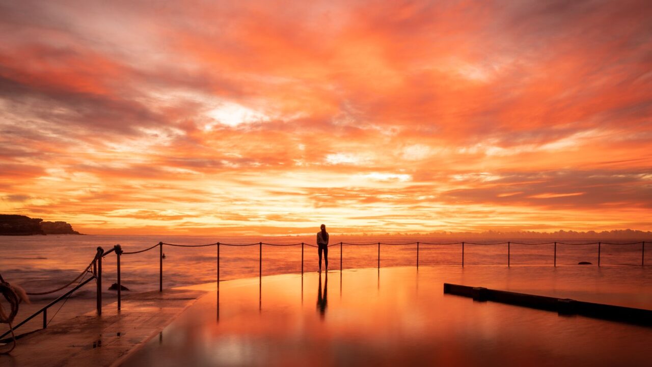 A red sunrise is pictured over Bronte Beach and pool, reflecting in the water.