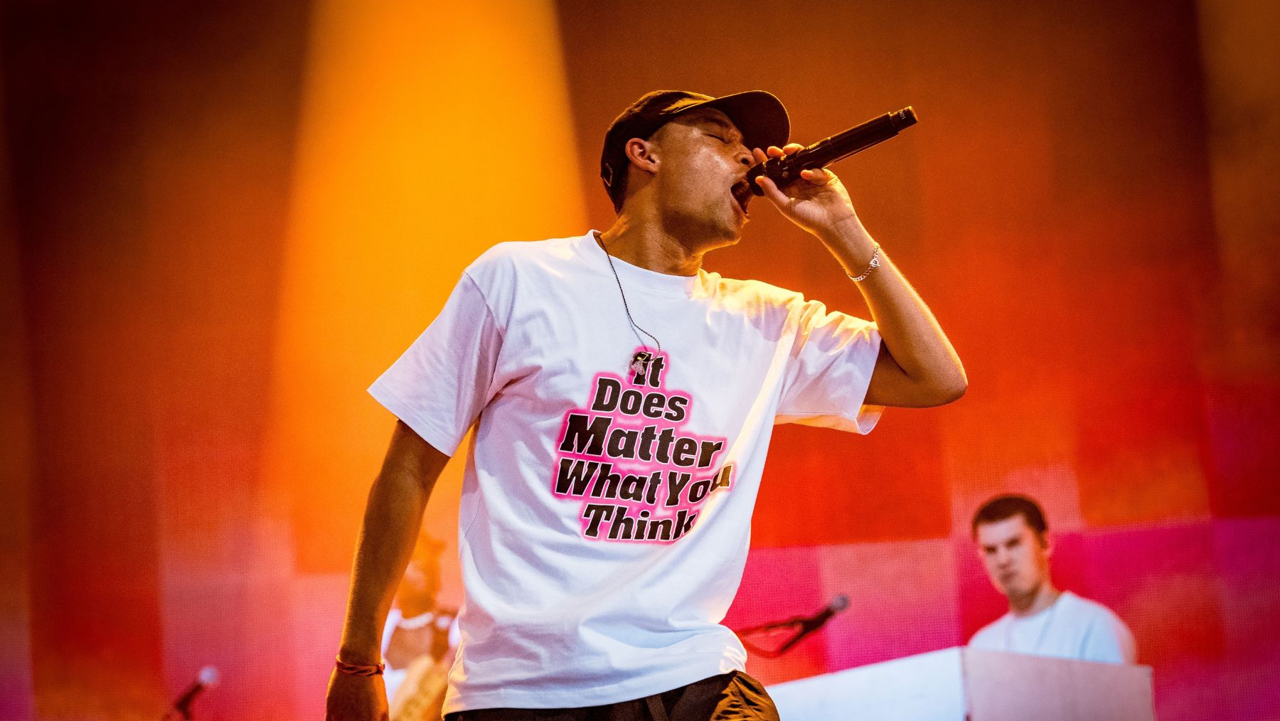 an artist singing into a microphone wearing a white graphic tshirt