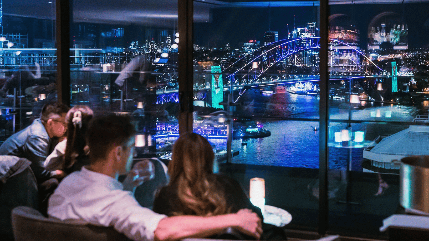A man and woman with their back to the camera look at a view of the Sydney Harbour Bridge at night during Vivid away from the crowds