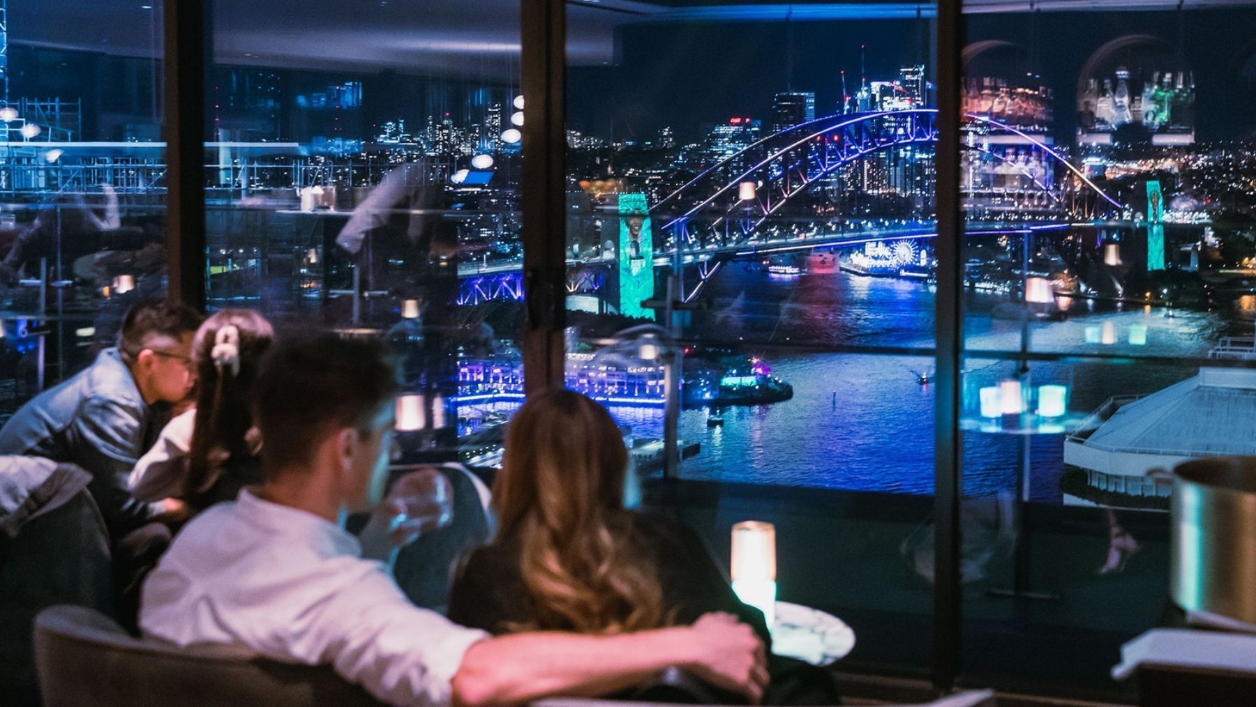A man and woman with their back to the camera look at a view of the Sydney Harbour Bridge at night during Vivid away from the crowds