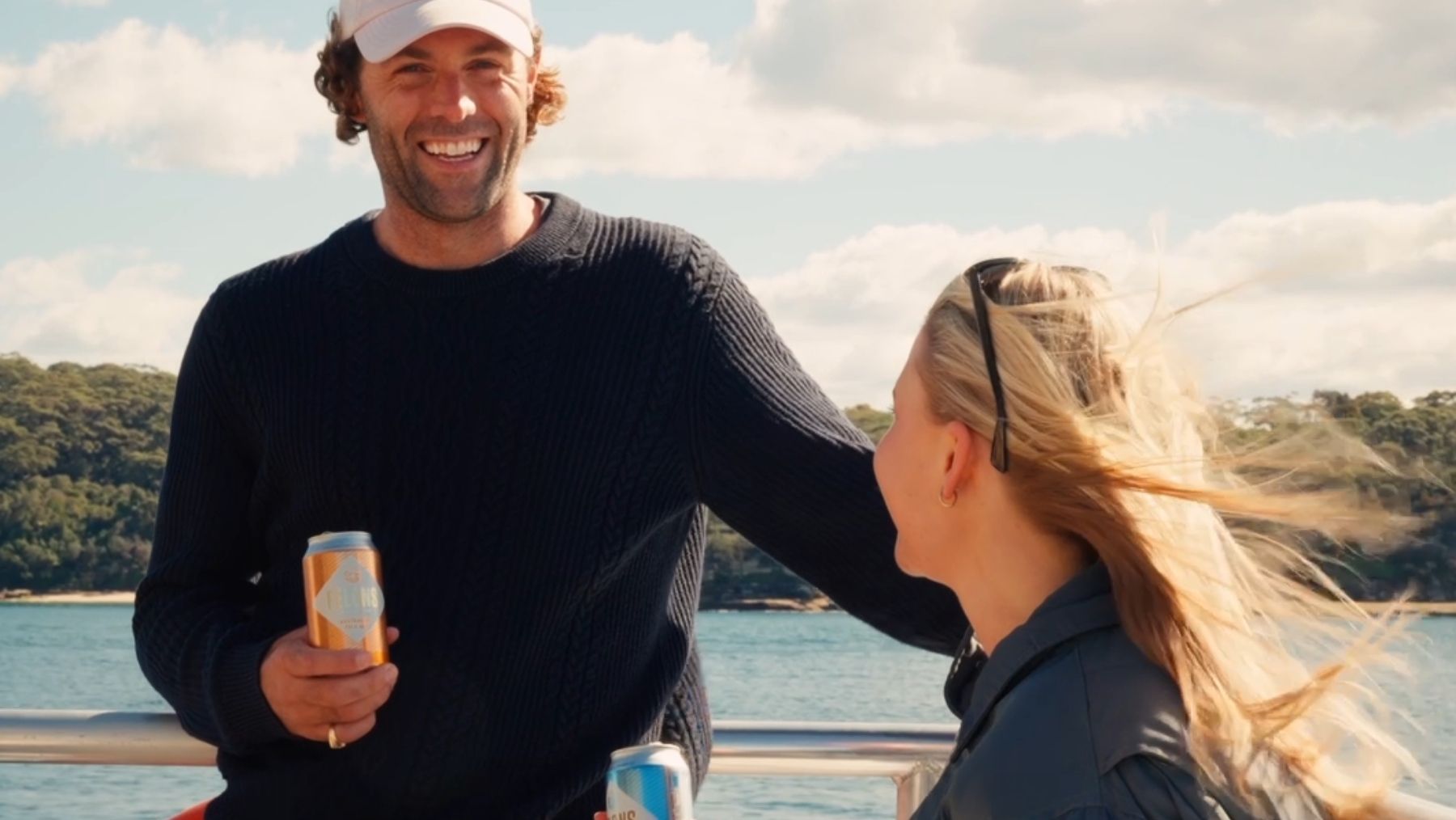 A man in a white hat, black jumper, holds a drink on a boat