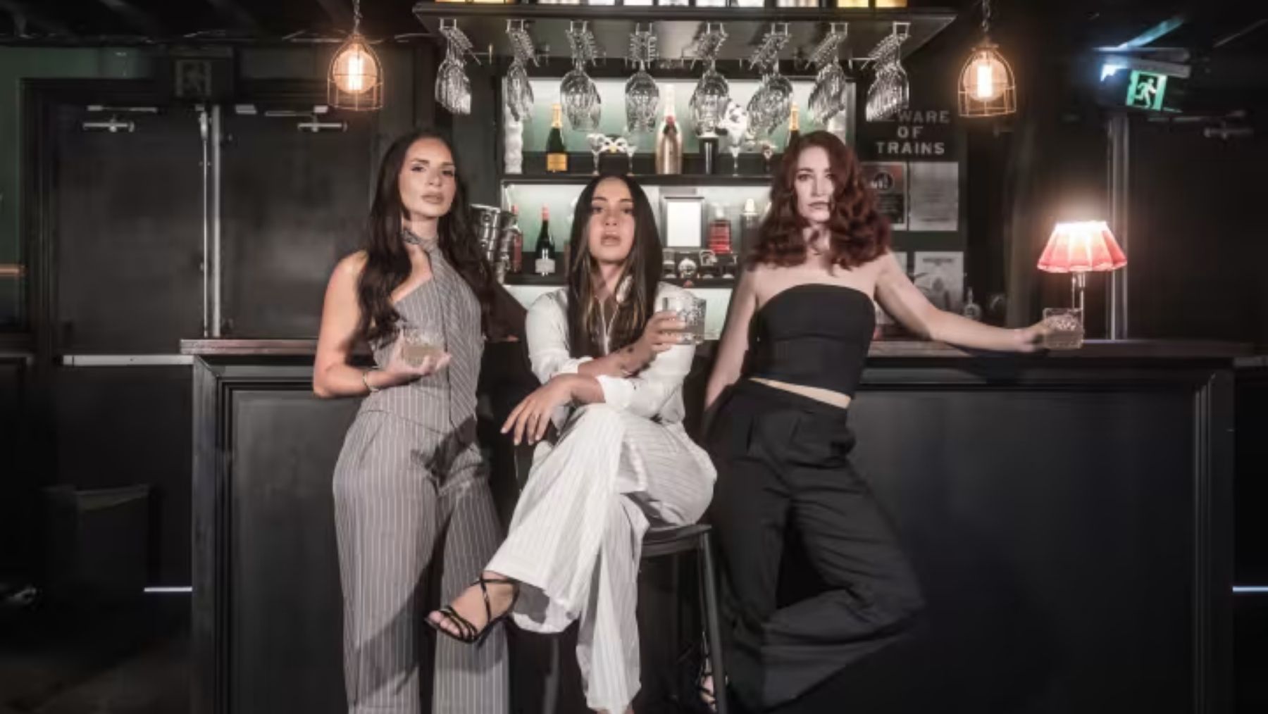 Three women sit and stand in front of a bar